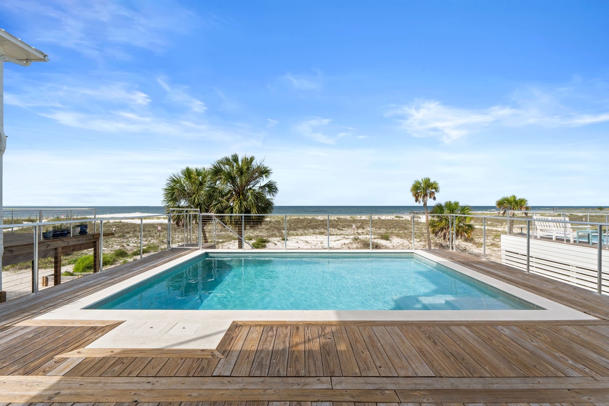 Private beachfront pool deck with direct beach access, palm-dotted dunes, and ocean views stretching to the horizon under clear blue skies.