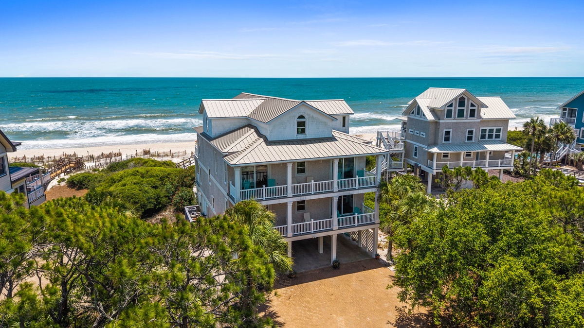 Aerial view of beachfront vacation rental surrounded by coastal greenery, with direct access to the sandy shore and turquoise waters beyond.