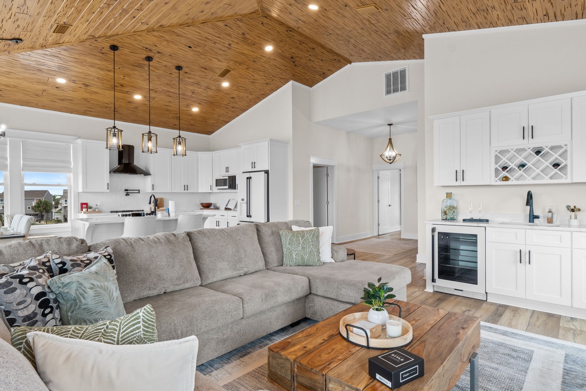 Unwind in your open-concept living space featuring soaring wood-planked vaulted ceilings, a plush sectional sofa, and a fully-equipped chef's kitchen with crisp white cabinetry and modern stainless appliances.