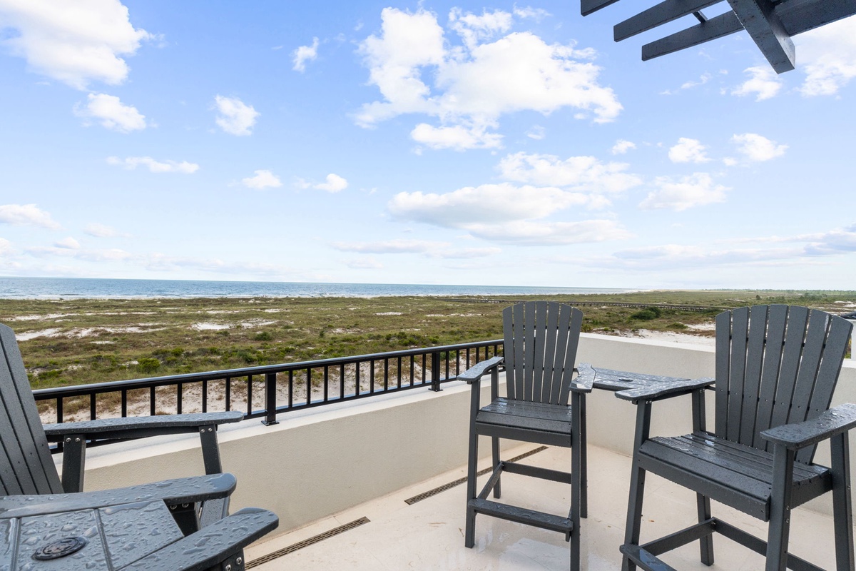 A private balcony with comfortable seating overlooks natural coastal dunes, offering sweeping views of the sea and surrounding landscape—a peaceful backdrop to your vacation retreat.