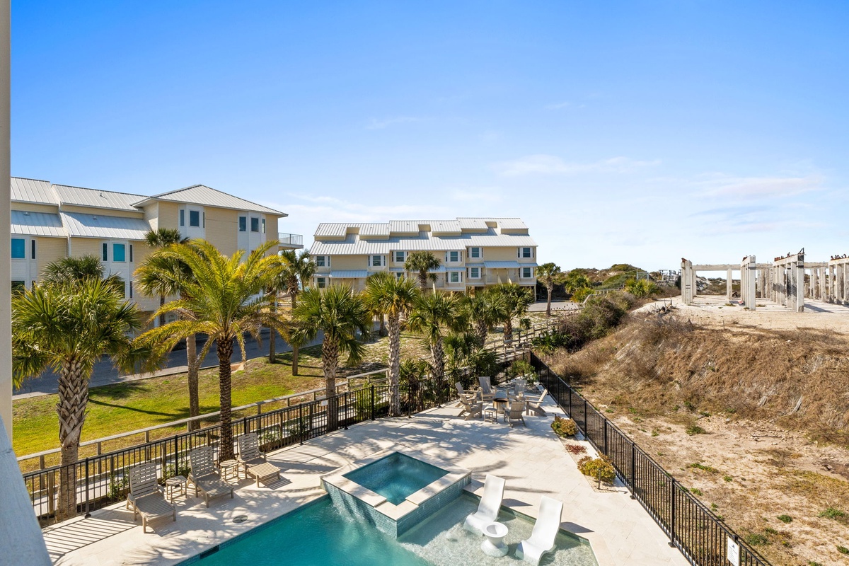 Beachfront resort complex with swimming pool, tropical palms, and direct beach access under brilliant blue skies.