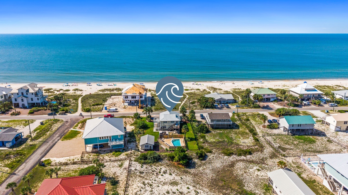 Aerial view of beachfront vacation homes and properties nestled along a pristine white-sand beach, with the turquoise Gulf waters stretching to the horizon.