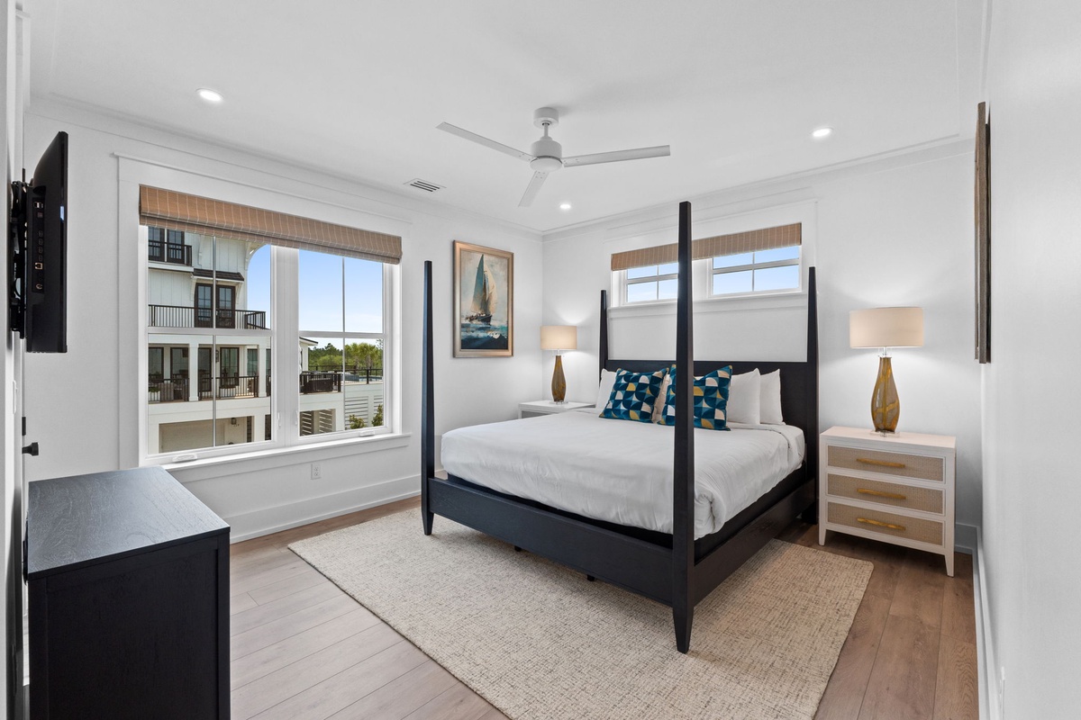 Unwind in your serene bedroom featuring a striking four-poster bed, coastal-inspired décor, and bright windows framing peaceful views of the waterfront community.