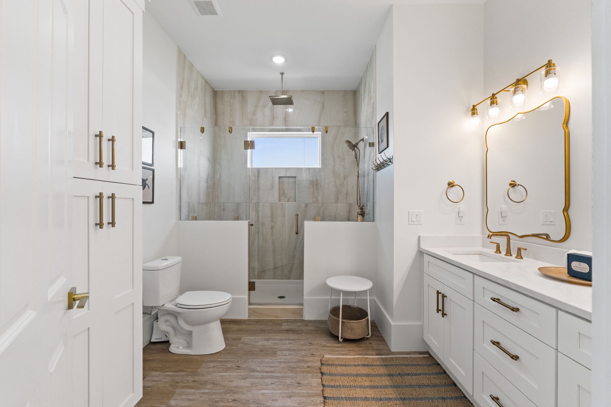 Step into your elegant en-suite bathroom featuring a spacious walk-in shower, beautiful vanity with gold accents, and thoughtful storage throughout.