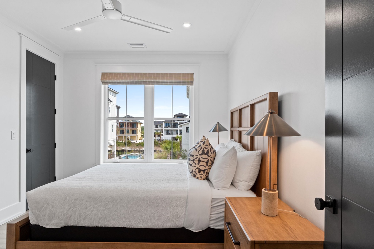 Wake up to a tranquil neighborhood view from your cozy bedroom, where modern coastal design meets comfort with soft linens and warm wood accents inviting restful nights.