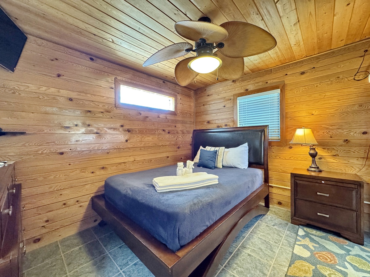 Unwind in your cozy log cabin bedroom with warm wood walls, a plush bed, and gentle ceiling fan breeze for perfect comfort.