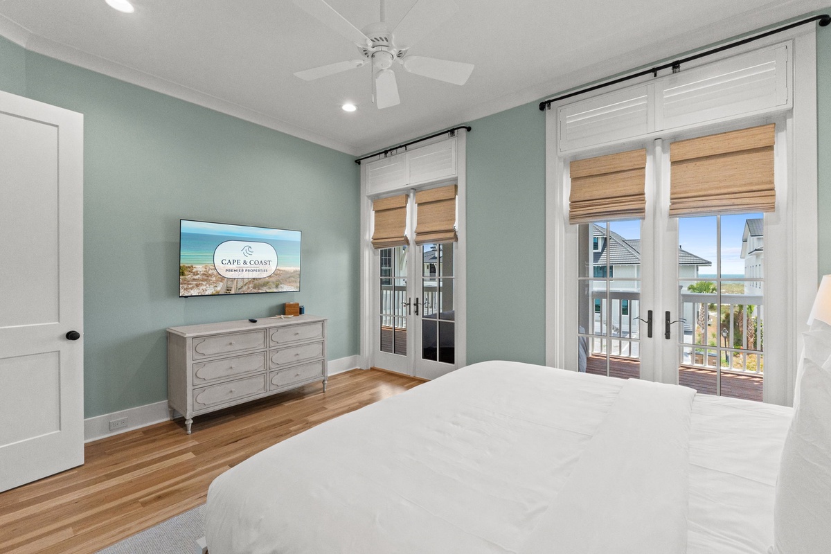 Wake up in your peaceful coastal bedroom with soothing seafoam walls and warm wood floors. Natural light and ocean breezes flow through your private balcony doors, while the ceiling fan keeps you perfectly comfortable.