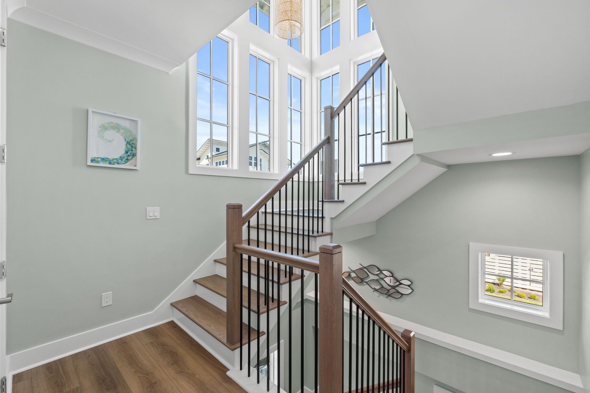 Bright, open stairway with soaring windows flooding your space with natural light. Rich wood steps and sleek railings guide you between floors, creating a warm and inviting entryway.