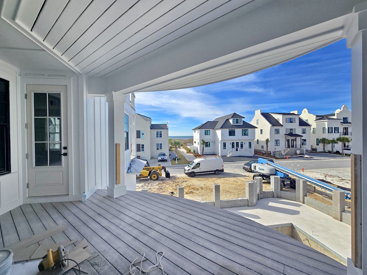 Covered deck with coastal community views featuring charming beach houses and blue skies beyond.