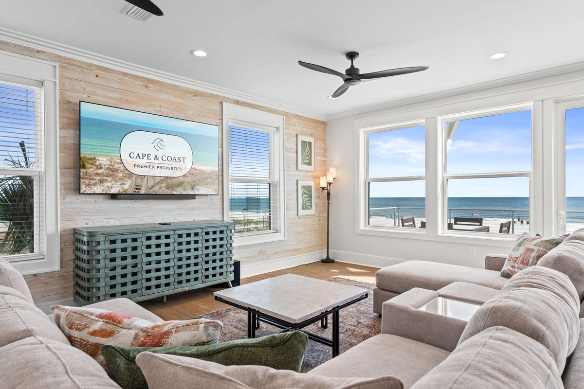 Unwind in your bright living room with stunning sea views through expansive windows, plush seating, and a ceiling fan to keep you comfortable during your beach getaway.