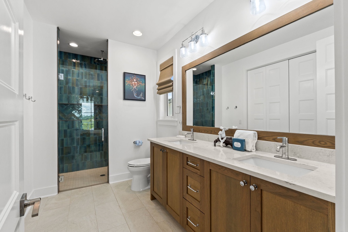 Refresh in your spacious bathroom, featuring a walk-in shower with stunning jewel-toned tile, dual vanities with marble countertops, and warm wood accents that create a spa-like retreat.