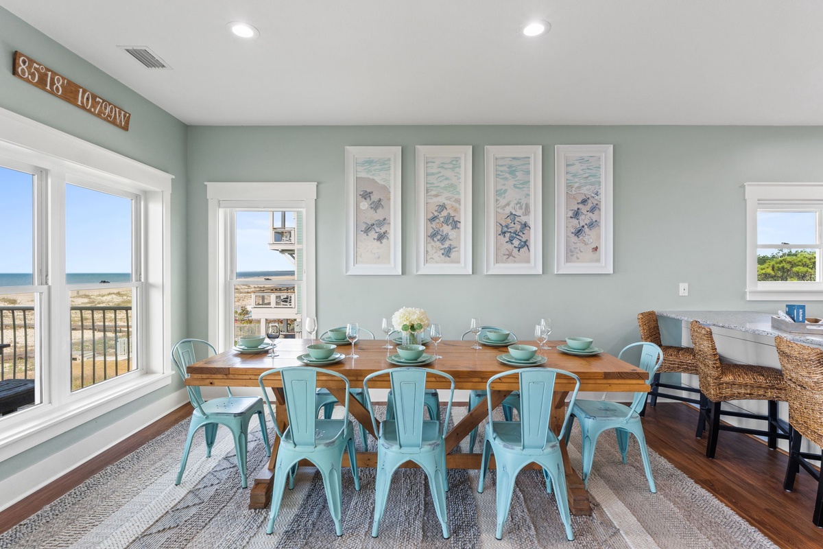 Gather around a sunlit dining table with coastal views streaming through the windows. The soothing sea-blue chairs and beach-themed artwork set a relaxed tone for memorable meals together.