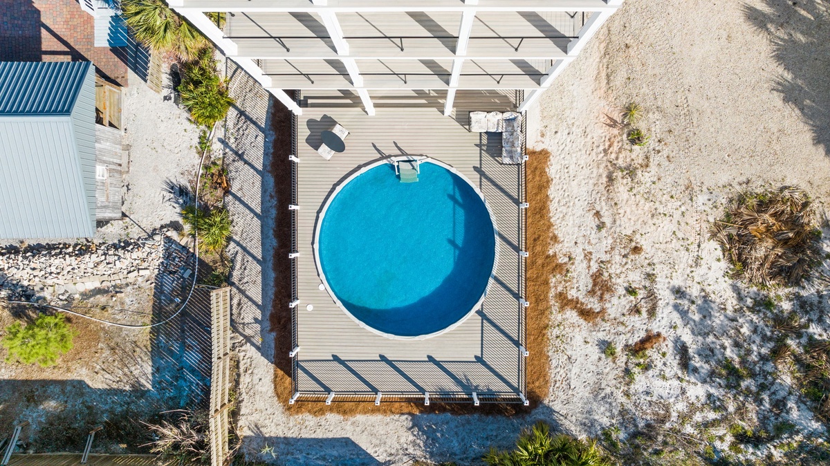 Aerial view of a modern circular pool with wooden decking, surrounded by natural coastal landscape and contemporary architecture.