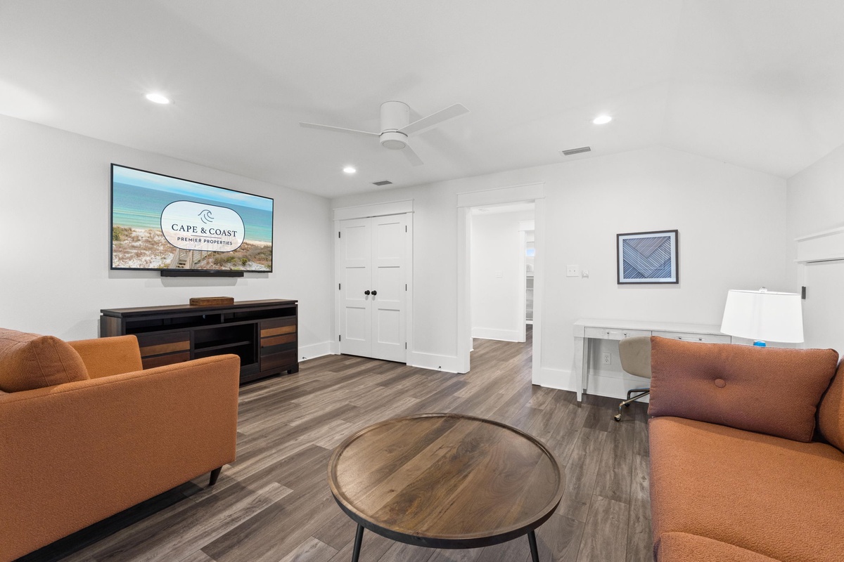 Relax in your spacious living area, featuring a large smart TV, stylish furnishings, and modern wood-look flooring—perfect for unwinding after a day at the beach.