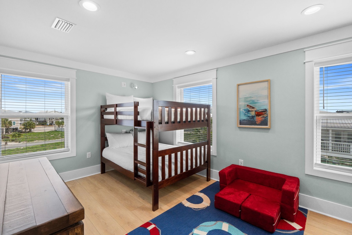 This bright, coastal-themed bunk room offers cozy sleeping for the kids with cheerful pops of color. Large windows frame peaceful neighborhood views, flooding the space with natural light.