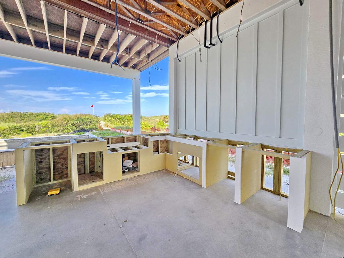 A property currently under construction with exposed beams and framing, offering views of the surrounding coastal landscape and dunes.