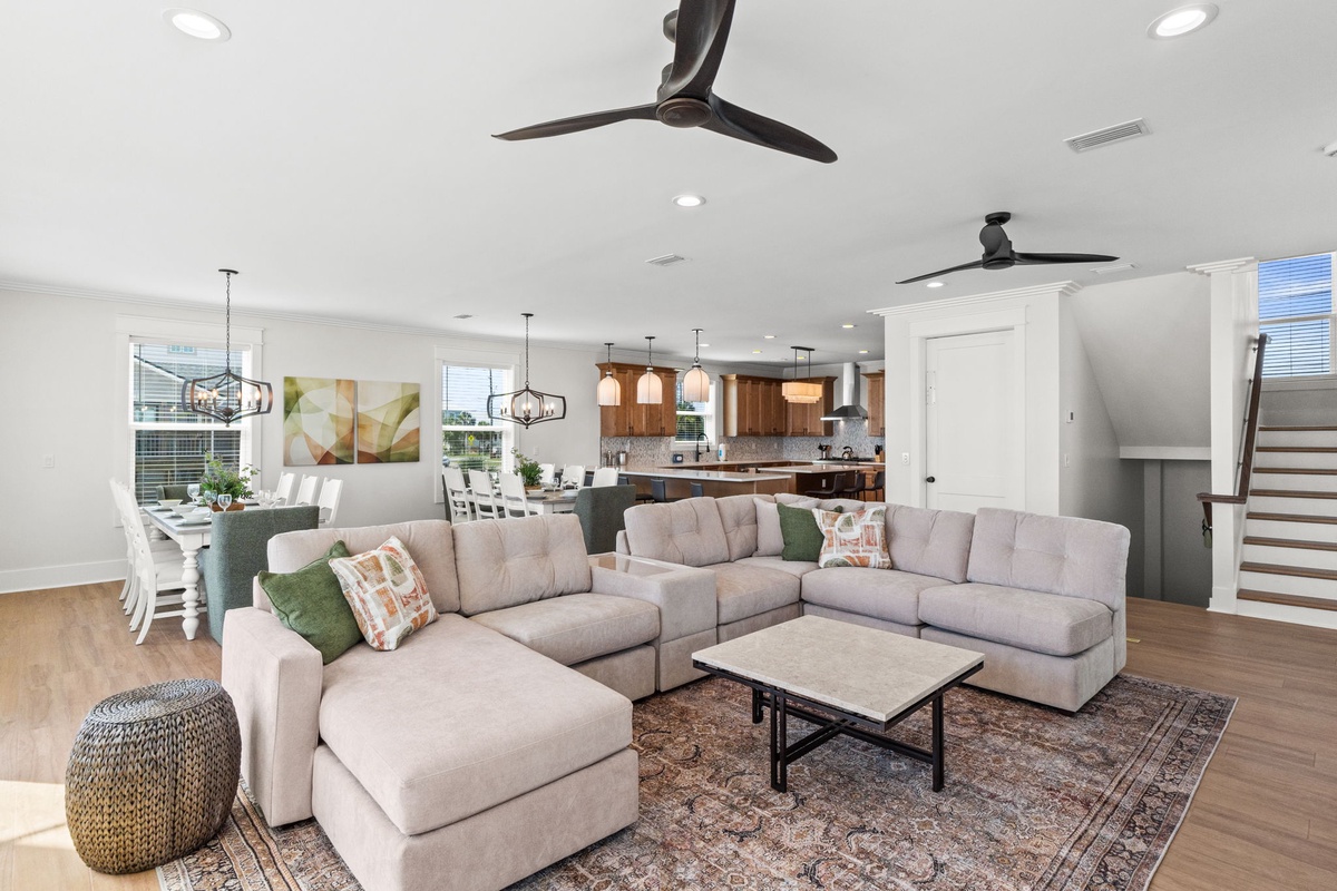 Settle into this open-concept living area with plush seating, modern ceiling fans, and seamless access to the fully-equipped kitchen and dining space for effortless gatherings.
