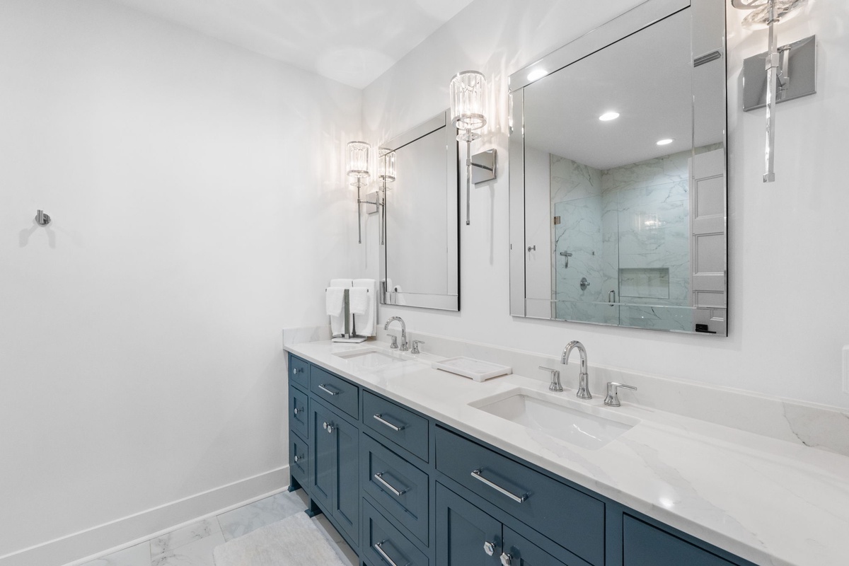 Indulge in your luxurious ensuite bathroom featuring elegant double vanities, pristine marble countertops, and a spacious walk-in shower behind gleaming glass doors.