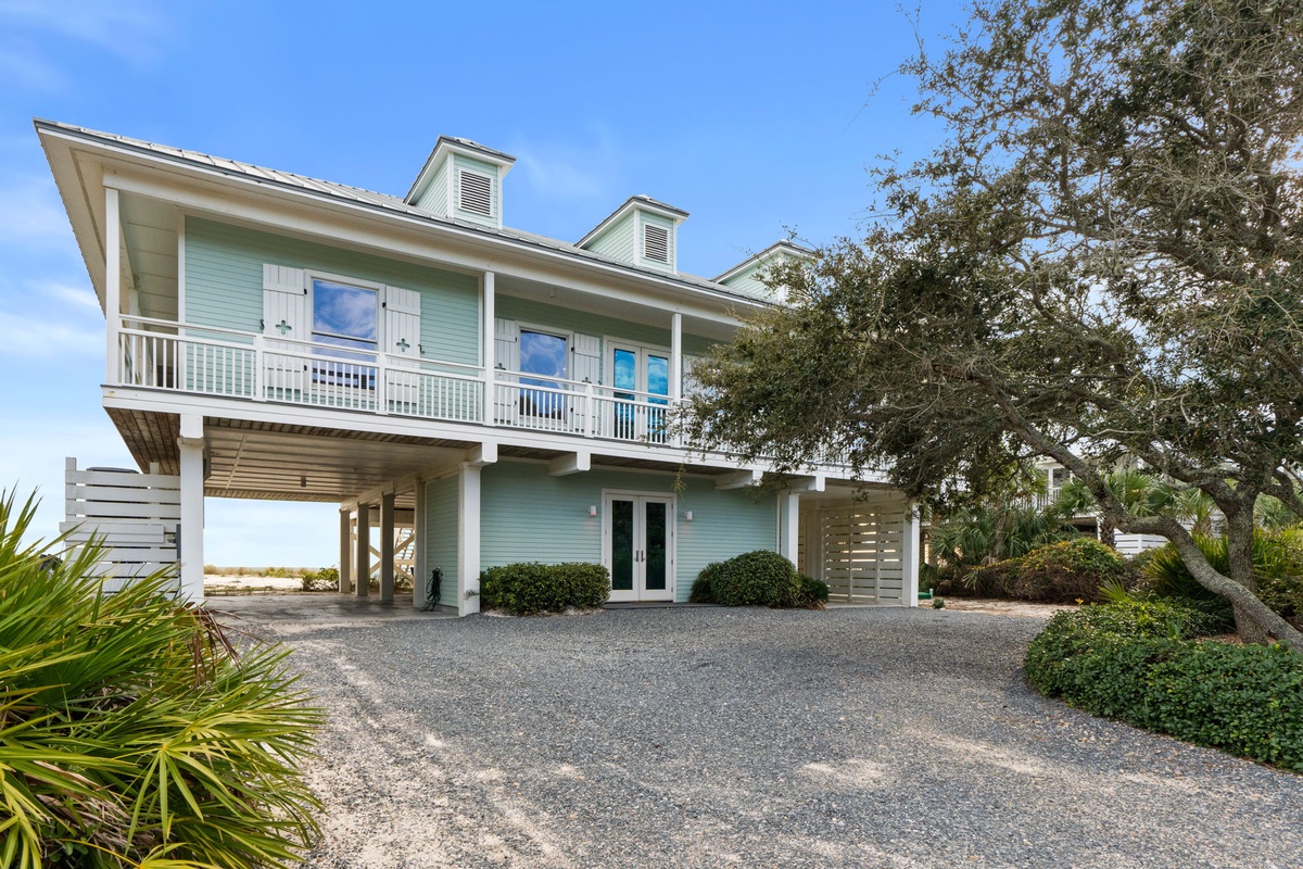 Charming coastal home with elevated design and covered parking, surrounded by mature landscaping and tropical plants.
