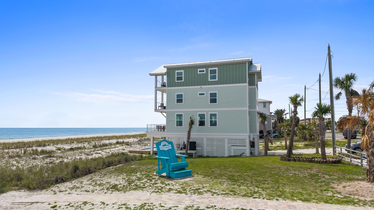 Beachfront property with direct sandy shore access, surrounded by swaying palms and coastal vegetation beneath clear skies.