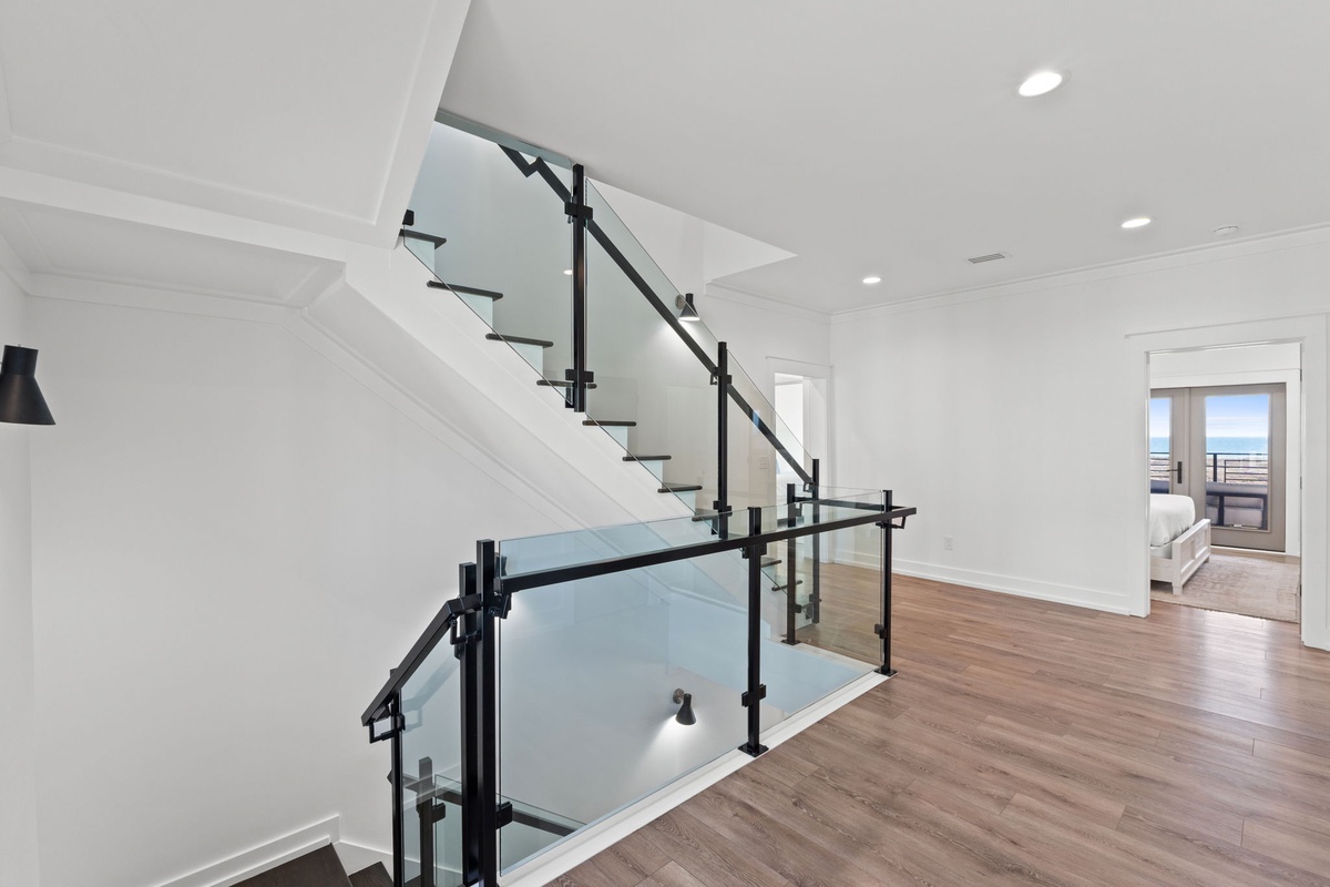 Step into your bright, modern sanctuary with sleek glass railings and warm hardwood floors that lead to your private bedroom retreat.