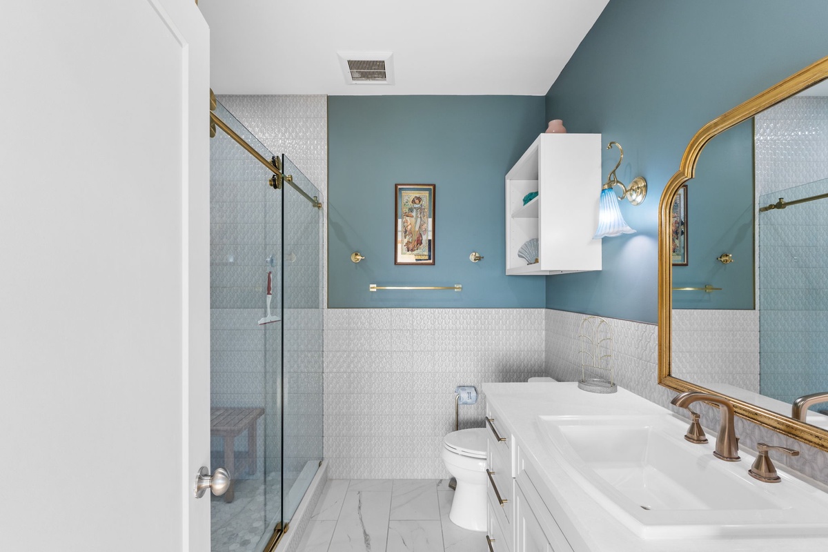 Unwind in your elegant bathroom with calming blue walls, gold accents, and a luxurious glass shower.