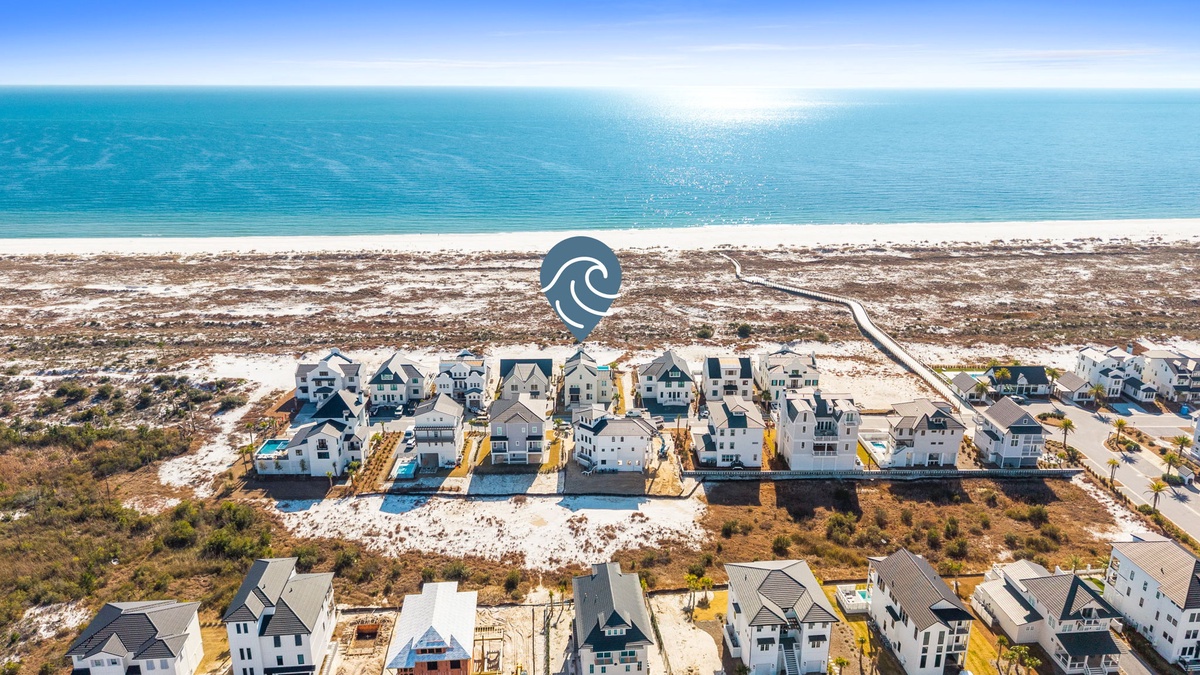 Aerial view of beachfront vacation rental community with pristine white sand beach and turquoise waters stretching to the horizon.