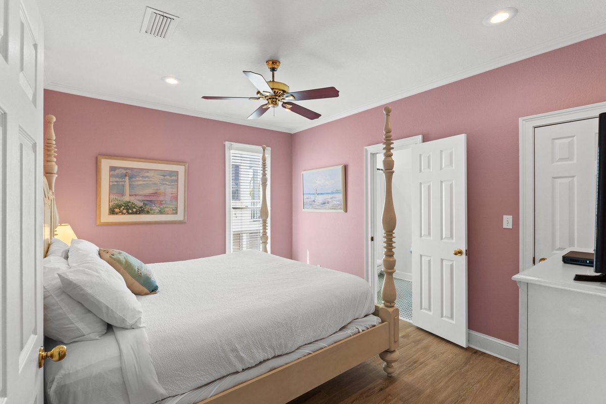 Rest in this charming bedroom with soft pink walls, elegant four-poster bed, and gentle ceiling fan creating your perfect retreat.