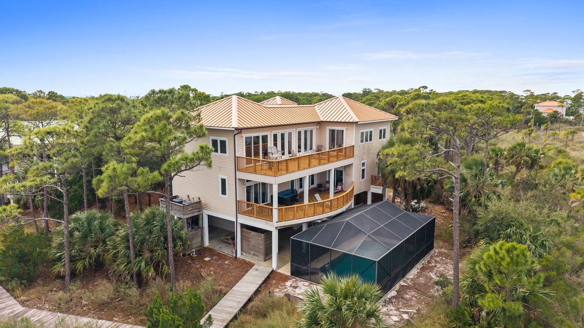 Modern three-story beach house with wraparound decks nestled among coastal palms and native vegetation.