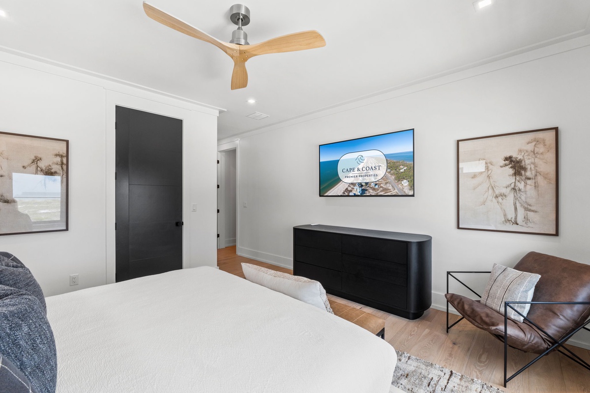 Unwind in your serene bedroom with a plush bed, stylish ceiling fan, smart TV, and coastal artwork creating a peaceful retreat for restful nights.