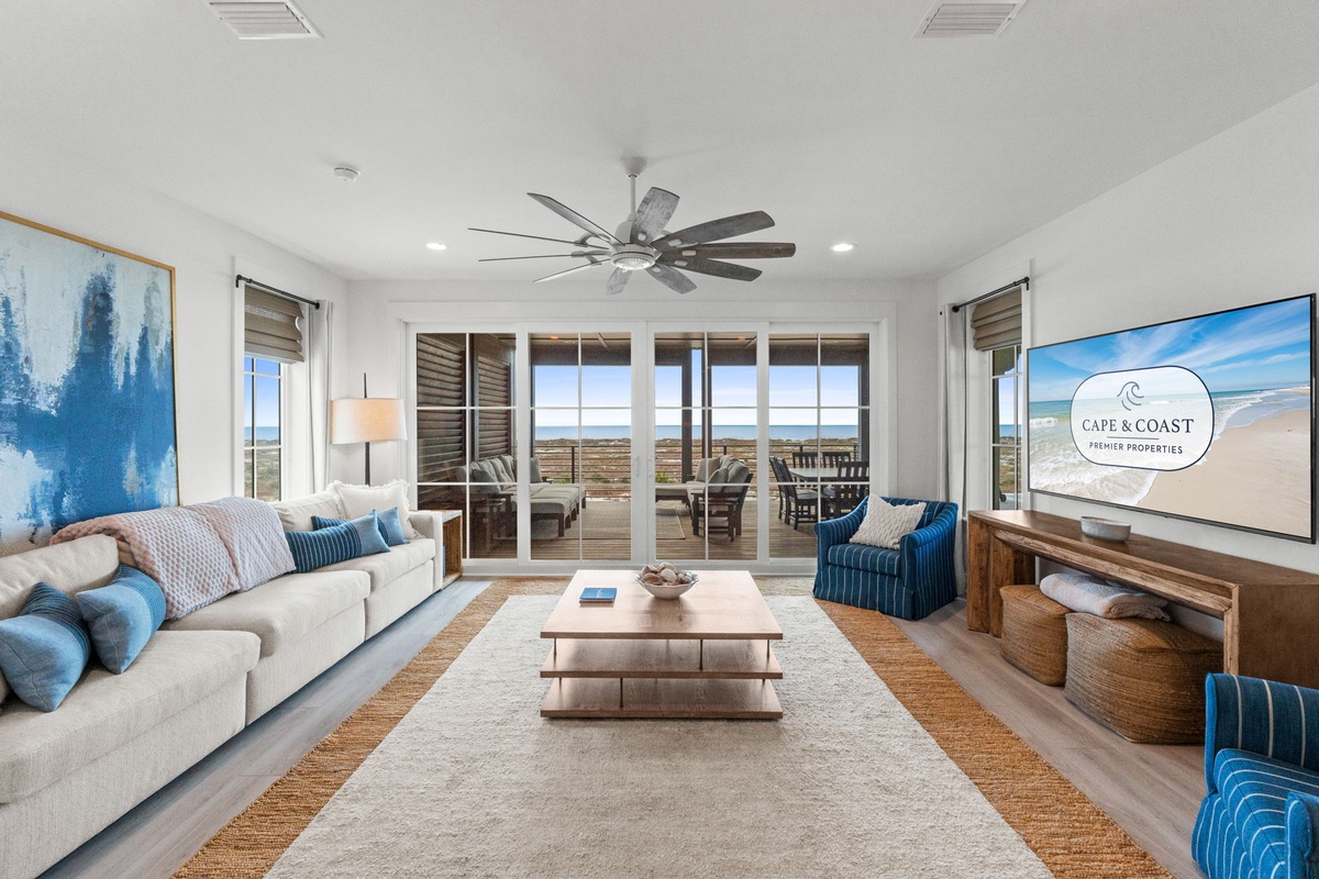 Relax in your spacious living room with ocean views through floor-to-ceiling windows. Blue coastal accents and comfy seating create the perfect beach retreat.