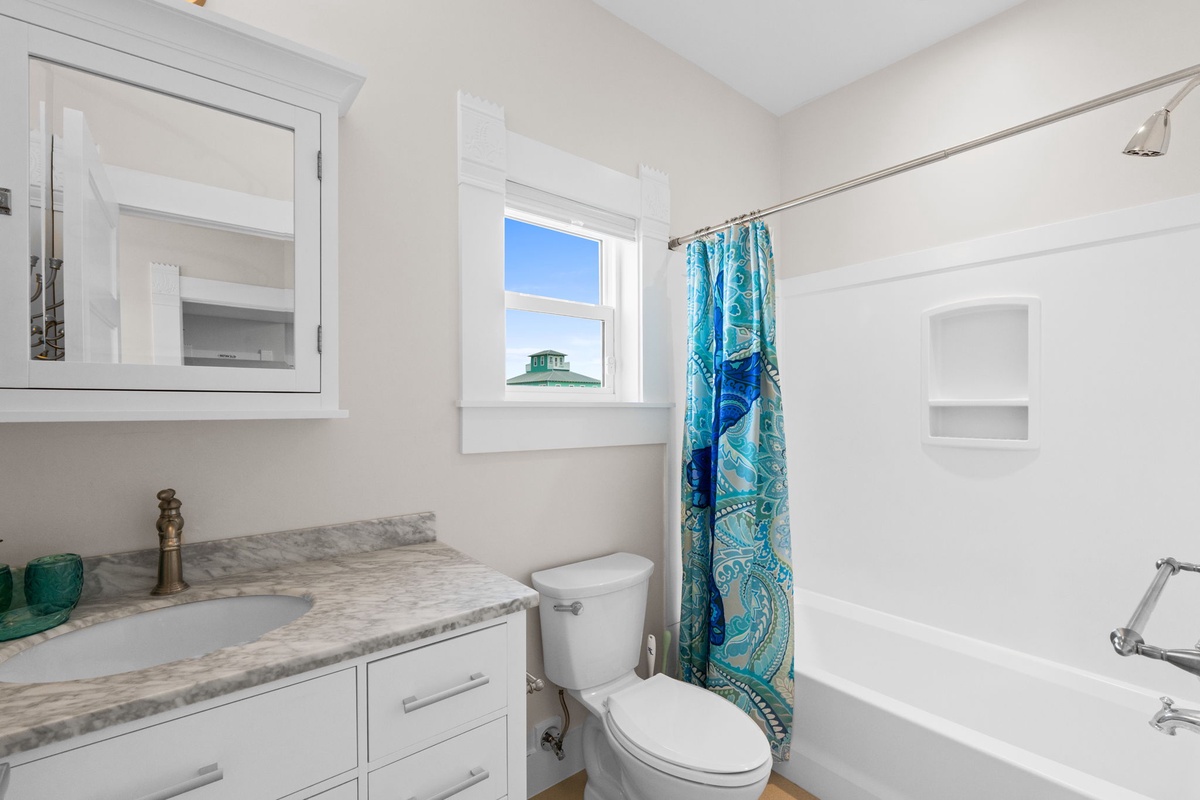 Step into your bright, clean bathroom featuring marble countertops, ample storage, and a cheerful ocean-themed shower curtain for your morning routine.