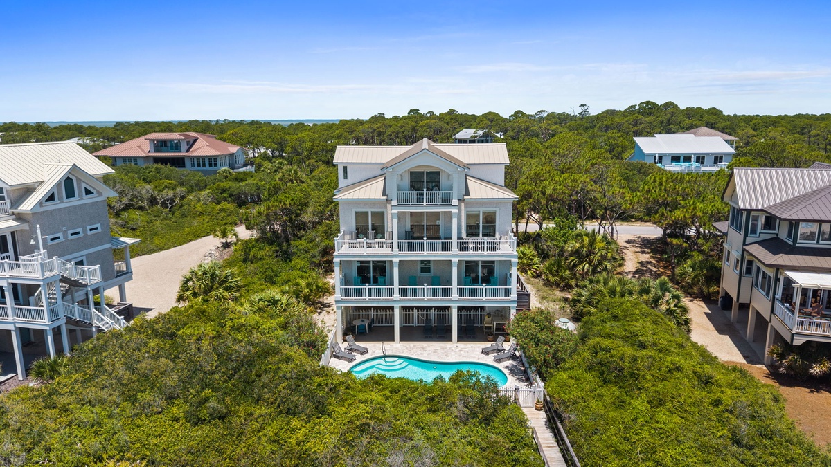 Aerial view of a coastal vacation home featuring a private pool, multiple balconies, and surrounded by lush natural vegetation in a serene beachside community.