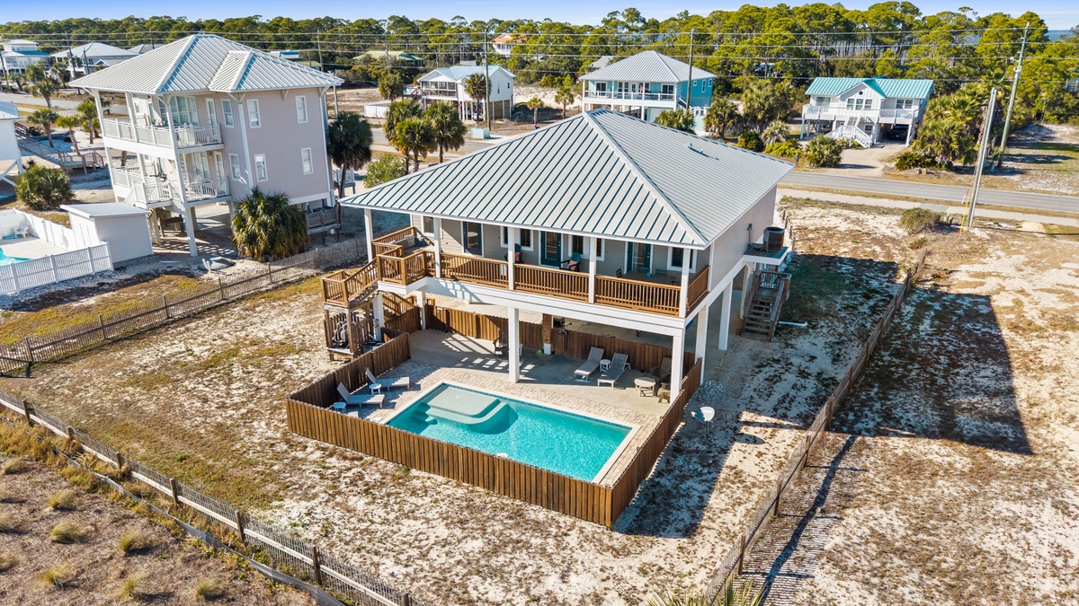 Aerial view showcases this coastal vacation home featuring private pool, elevated deck, and convenient beach access in a tranquil residential neighborhood.