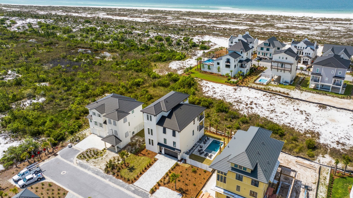 Aerial view of a residential neighborhood positioned between coastal dunes and pristine beachfront, offering convenient proximity to the water.