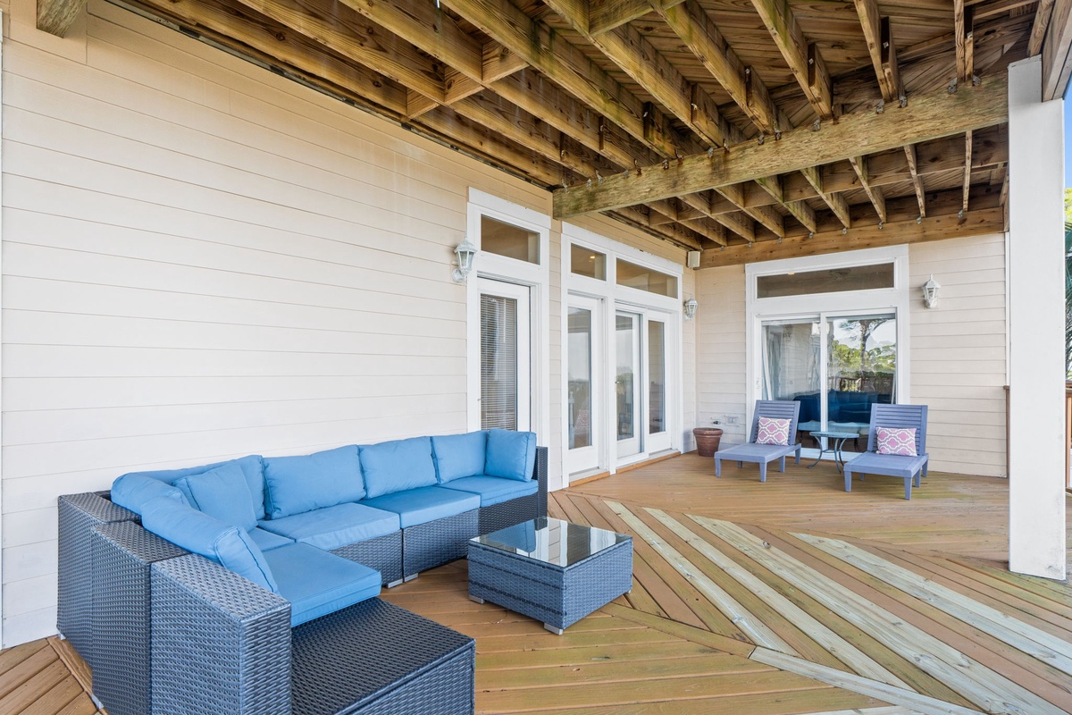 Relax on your spacious covered patio with plush blue seating, where rustic wooden beams create intimate gathering spots for morning coffee or evening conversations.