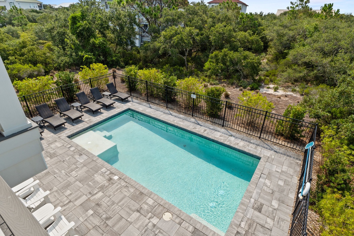 An elevated view reveals your private oasis: a sparkling pool framed by lush coastal greenery, with loungers ready for endless sunny afternoons.