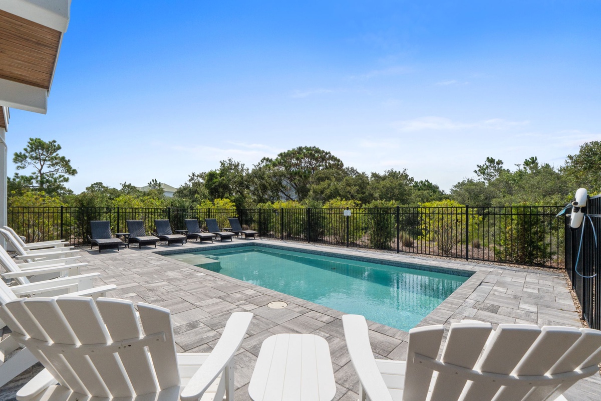 Private pool area surrounded by lush greenery and open sky, offering a peaceful retreat with plenty of lounge seating for sunny days.