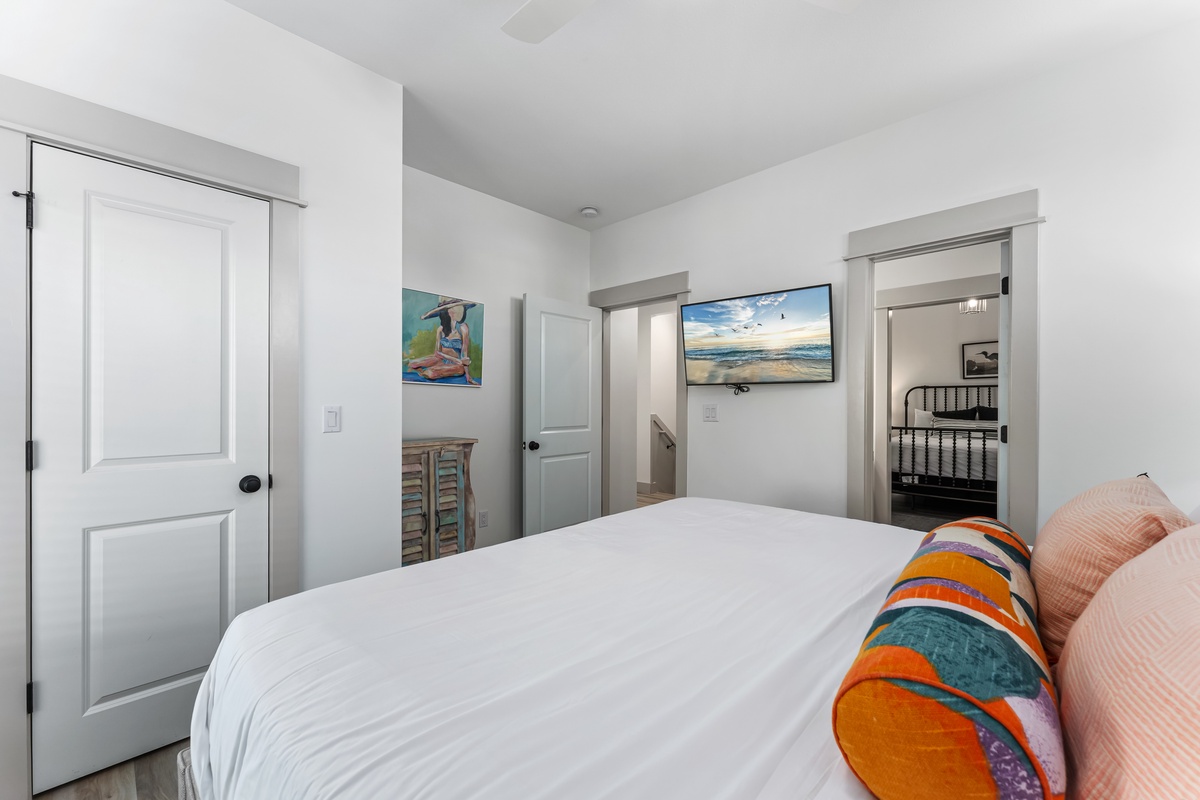 Unwind in your cozy bedroom featuring crisp white linens, vibrant coastal artwork, and a wall-mounted TV for relaxing evenings.