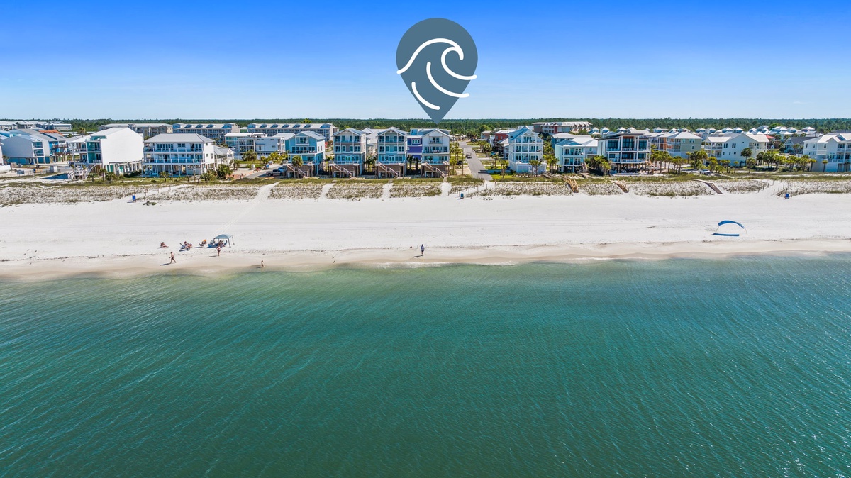 Aerial view of a beachfront vacation rental community with turquoise waters, pristine sand, and colorful beach homes lining the shore in a serene coastal neighborhood.