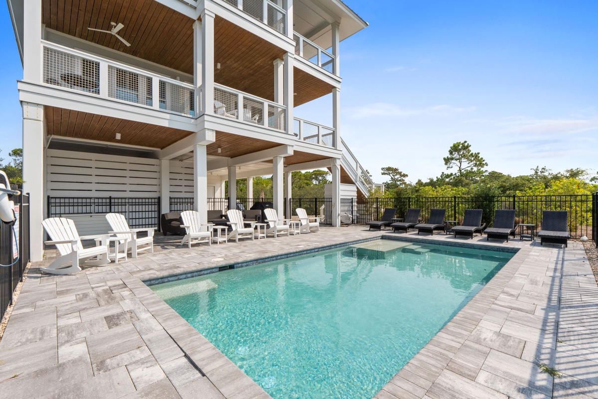 This property showcases a spacious elevated structure overlooking a private swimming pool area, surrounded by lush natural landscape and framed by clear blue skies.