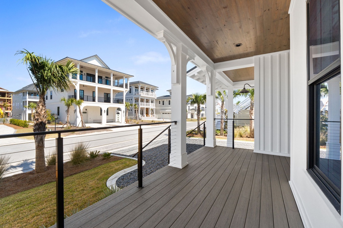 Covered porch with modern railings overlooks a peaceful residential neighborhood of coastal homes and palm trees.
