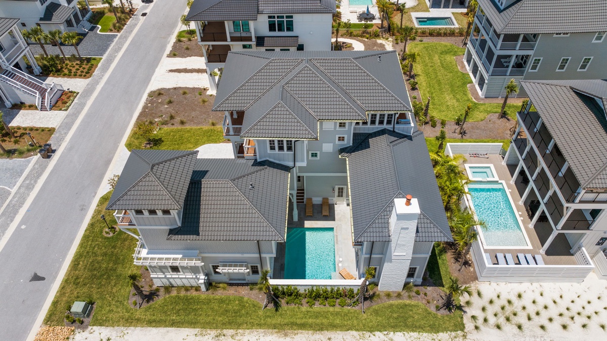 Aerial perspective of a modern vacation home in a newly developed neighborhood, featuring a private pool, spacious yards, and contemporary architecture. Located in a well-maintained residential community with easy street access.