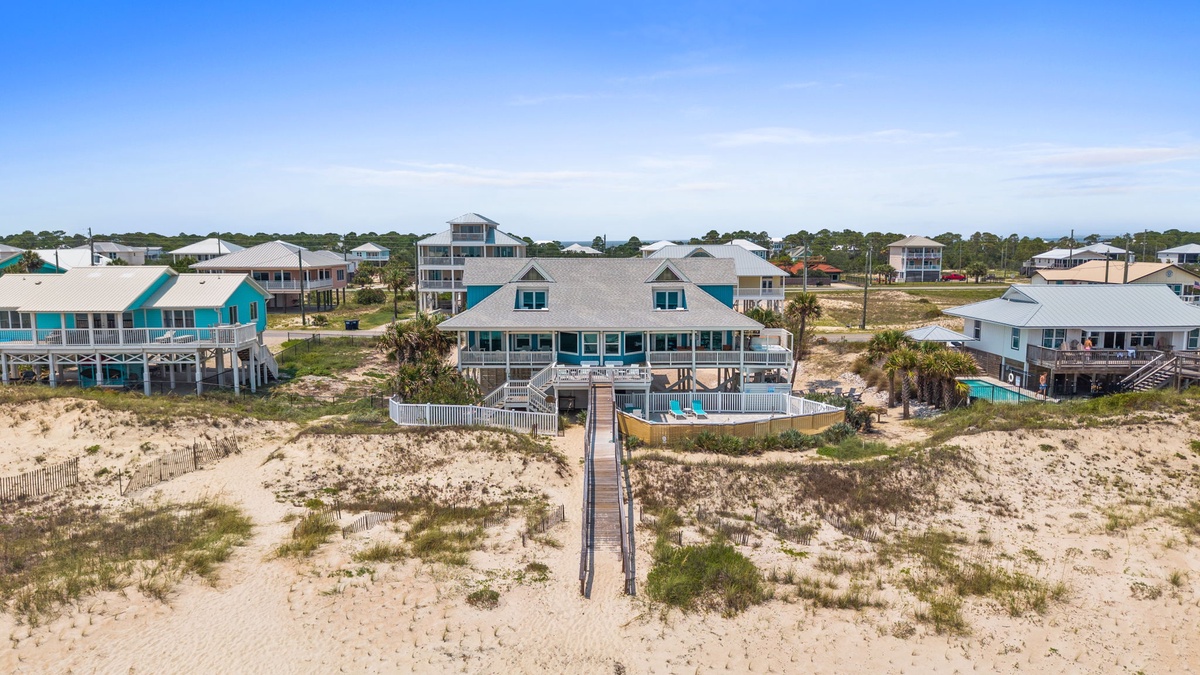 A beachfront property with direct sandy beach access via a private walkway, surrounded by coastal vegetation and neighboring vacation homes.