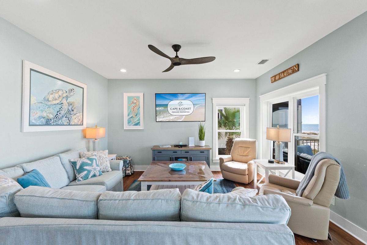 Sink into the plush sectional and breathe in the coastal calm. Your living space blends beachy charm with modern comfort, where ceiling fans keep you cool and ocean views invite daydreams beyond the open doorways.