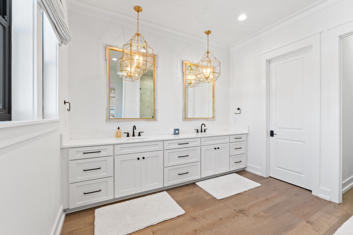 Your elegant dual-sink bathroom sparkles with golden fixtures and pristine white cabinetry, creating a spa-like retreat for your morning routine.