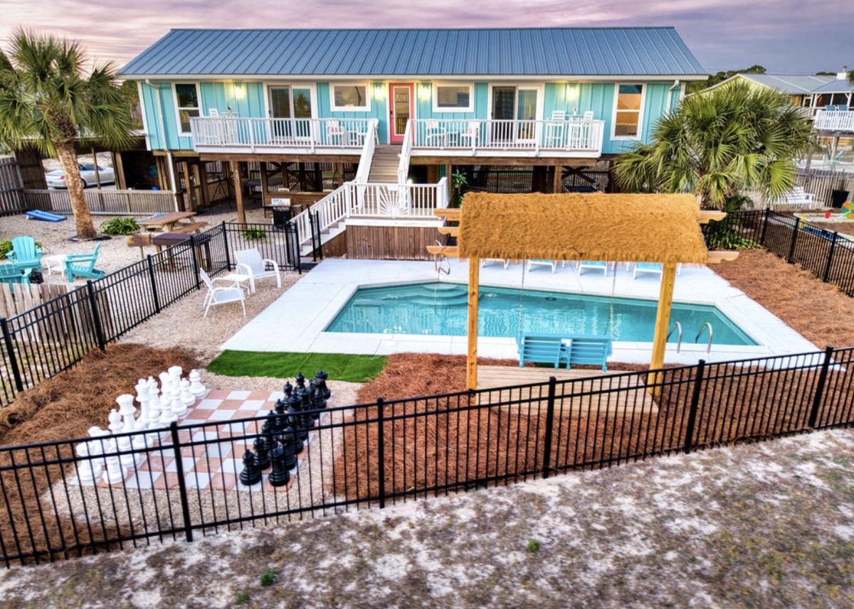 Bright turquoise beach house with private pool featuring thatched cabana, chess set, and tropical palms for coastal relaxation.