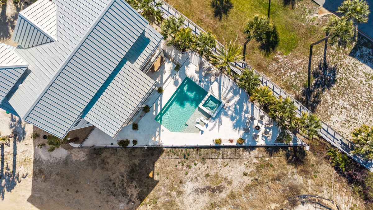 Stunning aerial view of a luxury vacation home featuring a pristine swimming pool surrounded by tropical palms and coastal landscaping.