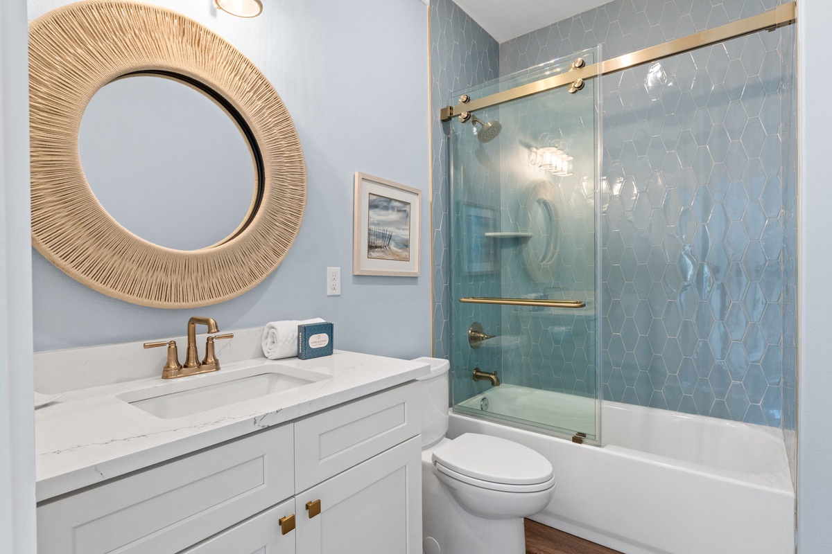 Step into your serene coastal-inspired bathroom, where soft blue hexagon tile meets warm brass accents. Unwind in the tub-shower combo after a day exploring, then prep for dinner at the elegant marble-topped vanity.