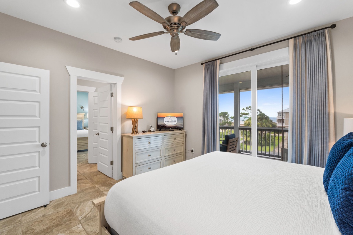 Drift off in your peaceful bedroom featuring a plush bed, ceiling fan, and private balcony with treetop views. Fresh coastal décor and ample storage make unpacking easy.